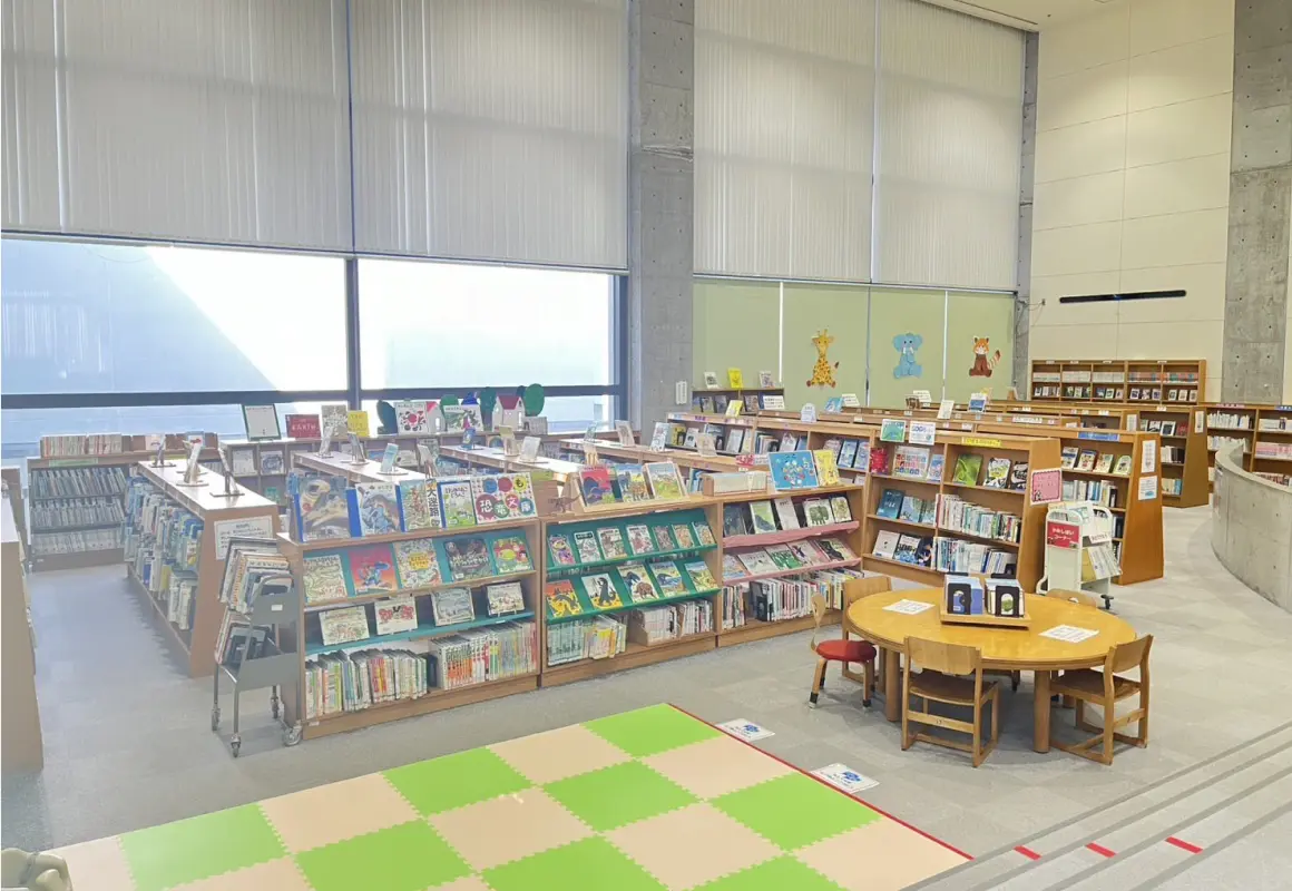 本棚が並び、ジョイントマットと丸テーブルが置かれた児童図書室